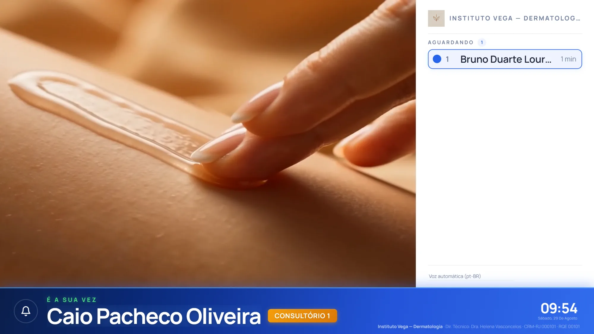 O painel de chamada numa TV da sala de espera: a faixa anuncia "É a sua vez — Caio Pacheco Oliveira, Consultório 1", com quem ainda aguarda na coluna ao lado